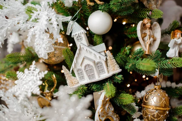 スタイリッシュなクリスマス ツリーのボールと天使の近くの緑の枝に掛かっている雪で覆われている家の形の装飾グッズ — ストック写真