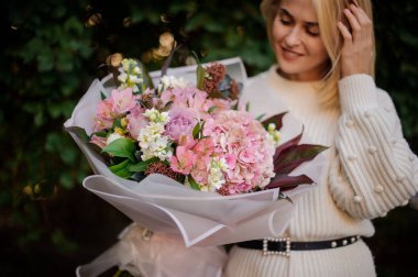 Onu elinde tutan güzel bir buket ihale pembe sonbahar çiçek Beyaz şeffaf kağıt beyaz sweather gülümseyen kız