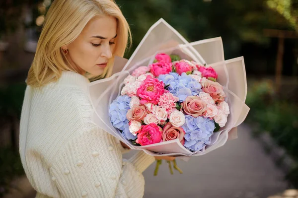 后视图女孩在白色毛衣握在她的手花束粉红色和蓝色的花朵在白色透明纸 — 图库照片