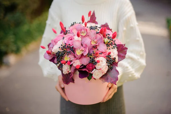 女孩在白色毛衣握在她的手一个巨大的粉红色的盒子不同的玫瑰花颜色的花朵装饰与叶子 — 图库照片