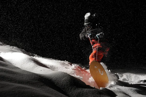黑色和橙色运动装活动滑雪板在漆黑的夜晚骑着雪粉山 — 图库照片