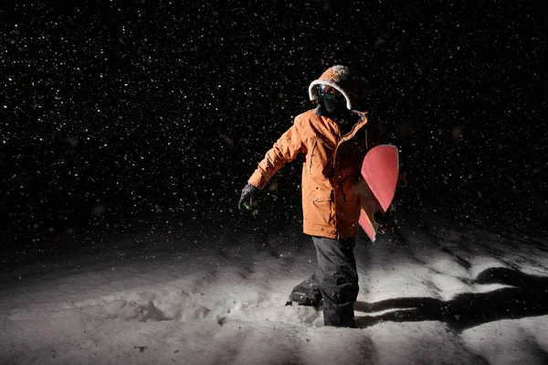 在橙色运动夹克的男性滑雪板在雪地上行走在晚上的手板 — 图库照片