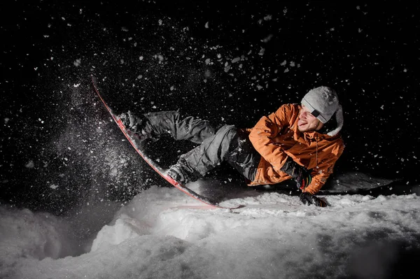 愉快的滑雪板在橙色夹克骑马与卡舌在一个下雪的粉山在黑暗的夜晚黑色背景 — 图库照片