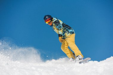 Mavi gökyüzüne karşı bir dağ eğim aşağı sürme parlak spor giyim genç aktif snowboarder