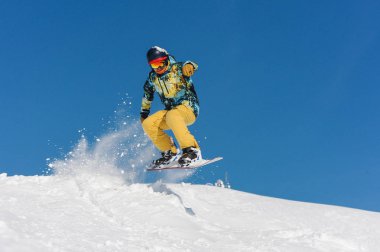 Mavi gökyüzüne karşı bir dağ yamacında kadar atlama parlak spor giyim genç aktif snowboarder