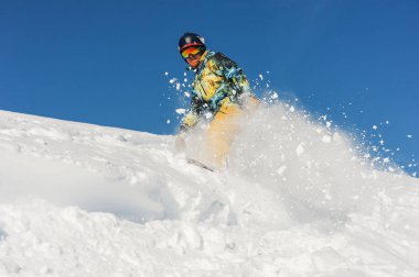 Gürcistan'daki mavi gökyüzü karşı bir toz dağ eğim aşağı sürme parlak spor giyim aktif profesyonel snowboarder