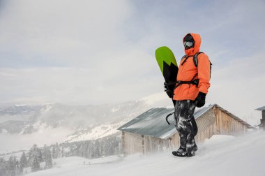 Adam Goderzi, Gürcistan'daki popüler turistik tatil irtifa evin arka plan üzerinde dağ tepe üzerinde elinde snowboard ile ayakta