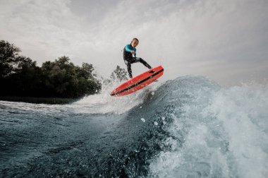 Etkin mutlu çocuk çocuk mayo wakesurfing mavi yüksek dalga aşağı turuncu gemide giyinmiş