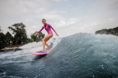 Aktif genç kız nehrin arka planda gökyüzü ve ağaçlar sağlıklı yaz sahip turuncu wakeboard üzerinde ayakta