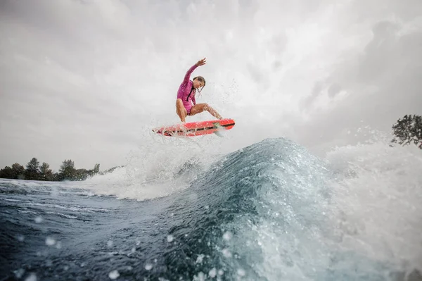 アクティブな女性 Wakesurfer は曇りの日に青空青いしぶき波をジャンプ ピンクの水着に身を包んだ — ストック写真