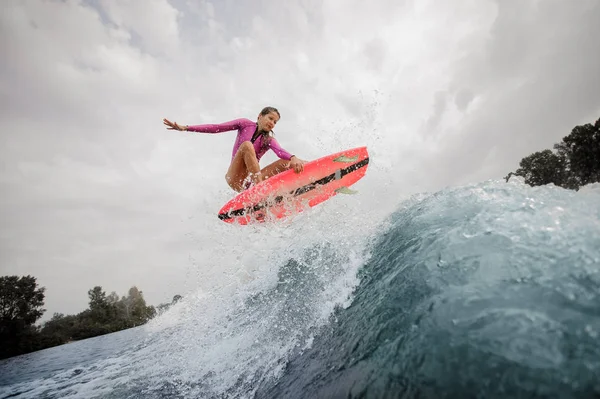 アクティブな若い女性 Wakesurfer は曇りの日に青空青いしぶき波をジャンプ ピンクの水着に身を包んだ — ストック写真