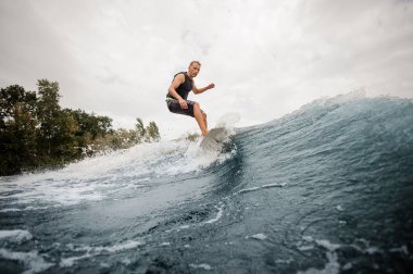 Yan görünümü etkin çocuk sağlıklı yaz Nehri arka planda gökyüzü ve ağaçlar üzerinde sahip wakeboard sürme