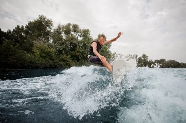 Etkin adam arka planda gökyüzü ve ağaçlar Nehri üzerinde sağlıklı yaz sahip yüksek dalga wakeboard sürme