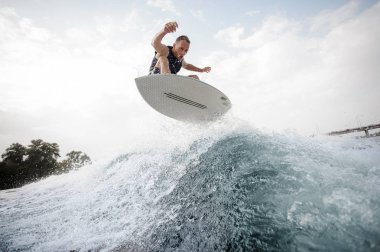 Arka planda gökyüzü ve Köprü Nehri üzerindeki mavi dalga beyaz wakeboard etkin delikanlı yapım atlama