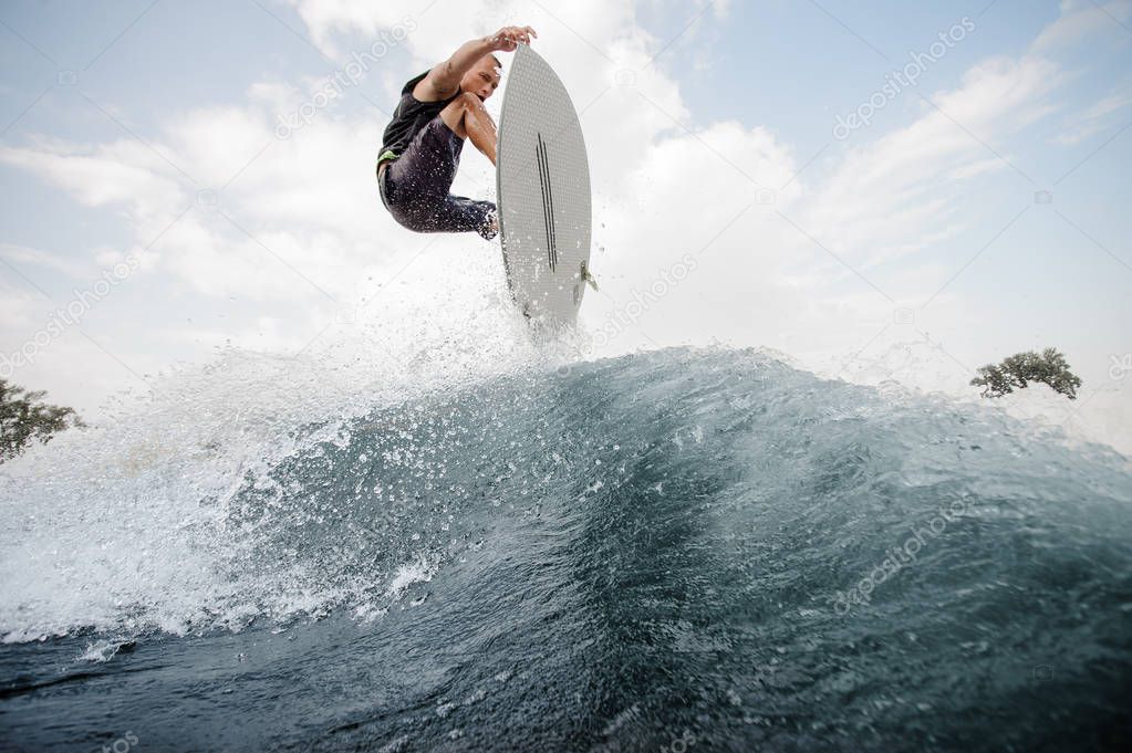 Young active man jumping up on the white wakeboard on the high blue wave on the river on the background of sky