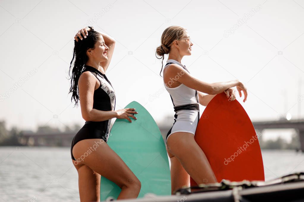 Two attractive girls in the black and white and red swimsuit standing with the wakeboards