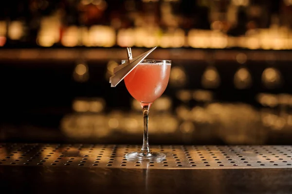 Bicchiere di un delizioso cocktail decorato con un aereo di carta in piedi sul bancone del bar — Foto Stock