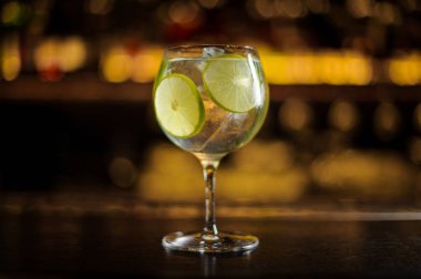 Cin tonik kokteyl dekore edilmiş limonlu dilimler çelik çubuk üzerinde duran counter üzerinde arka plan bulanık