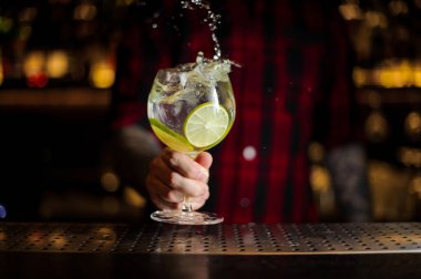 Bir cin tonik sıçrama kokteyl yapmak barmen dekore edilmiş kireç dilimleri çelik bar counter üzerinde arka plan bulanık