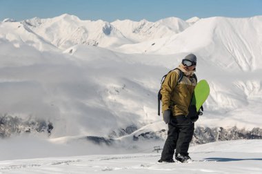 Dağ snowboard ile ayakta ve kamera popüler turistik tatil bakarak bir adam