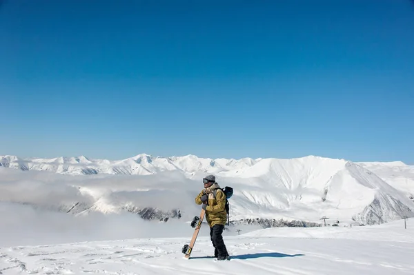 男子拿着滑雪板站在山上 望着佐治亚州热门旅游胜地的远处 — 图库照片