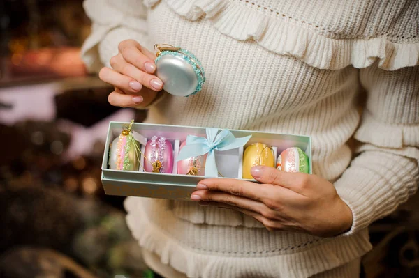 Menina segurando um macaroon azul e caixa de muitas lâmpadas de brinquedo brilhantes de cores diferentes — Fotografia de Stock