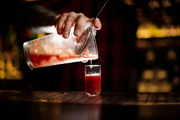 Barman pouring alcoholic tomato cocktail into a glass shot
