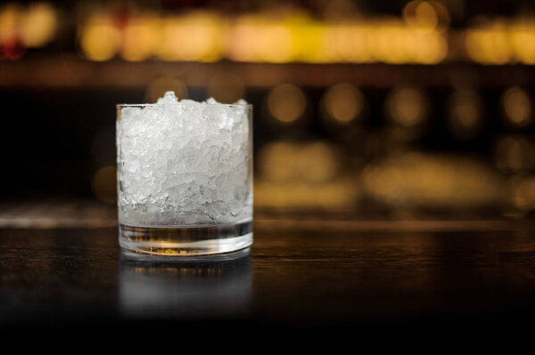 Cocktail glass with ice cubes on the bar counter in blurred background