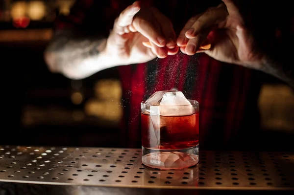 Cantinero rociando jugo de cáscara de naranja en una copa de cóctel llena de fuerte bebida de whisky — Foto de Stock