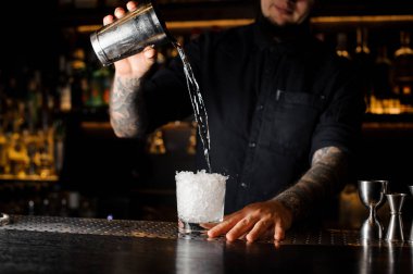 Profesyonel barmen çubuğunda ezilmiş buz cam çelik shaker dan bir içecek dökülen sayaç