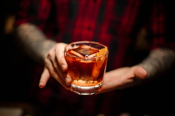 Barman tatuado sosteniendo una copa de cóctel con whisky — Foto de Stock