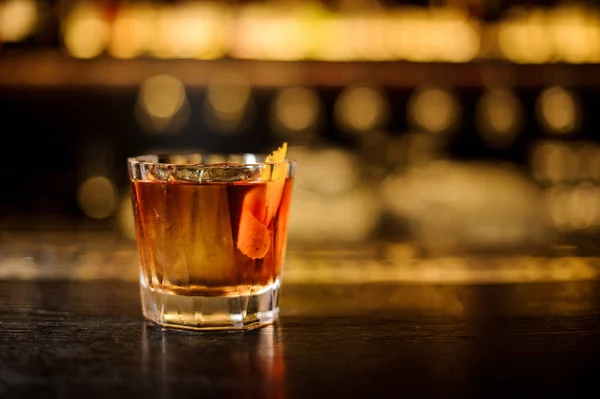 Glass filled with strong cocktail with whiskey on the bar against the lights — Stock Photo, Image