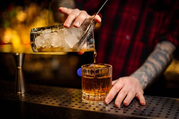 Cantinero vertiendo alcohol fuerte en una copa de cóctel con cubo de hielo usando un colador — Foto de Stock