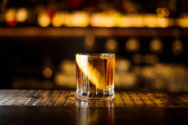 Elegant low glass filled with strong cocktail with light whiskey on the bar against the golden lights — Stock Photo, Image