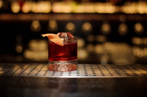 Bicchiere di cocktail Boulevardier con scorza d'arancia e cubetto di ghiaccio sul bancone del bar in legno d'acciaio — Foto Stock