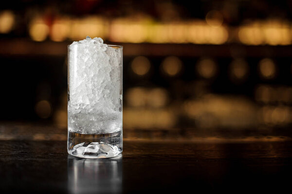 Tall glass of crushed ice standing on the bar counter