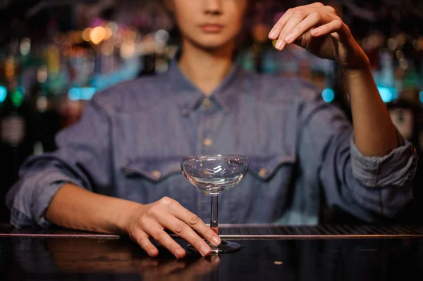 Female bartender holding an empty cocktail glass standing on the bar counter — Stock Photo, Image