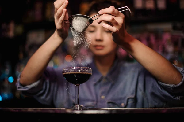 Женщина-бармен добавляет в коктейль коричневый алкоголь порошок через фильтр на барной стойке — стоковое фото