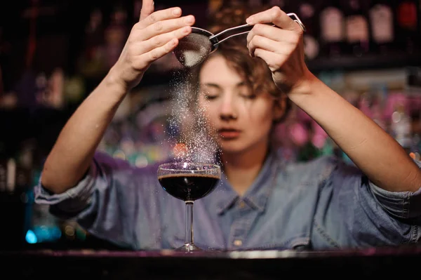 Бармен девушка добавляет в коктейль с коричневым спиртом порох через фильтр на барной стойке — стоковое фото