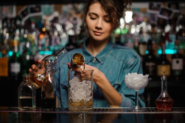 Cantinera hembra vertiendo a la taza de vidrio medidor con cubitos de hielo una bebida alcohólica de jigger — Foto de Stock