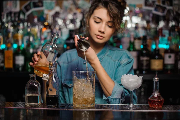 Menina derramando para o copo de vidro de medição com cubos de gelo uma bebida alcoólica de jigger — Fotografia de Stock