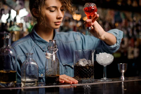 Женщина-бармен наливает в мерную чашку с кубиками льда красный горький из стеклянной бутылки — стоковое фото