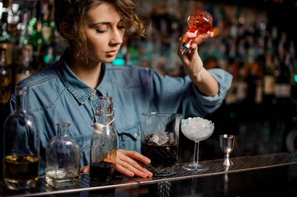 Garota barman derramando para o copo de medição com cubos de gelo um amargo vermelho da garrafa de vidro — Fotografia de Stock