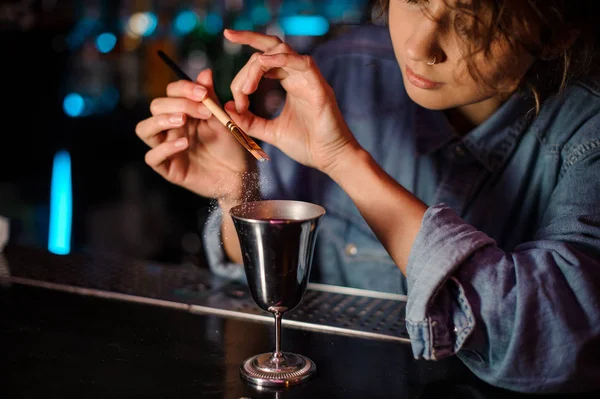 Bartender girl adding a glitter from the brush to a cocktail glass with alcoholic drink — Stock Photo, Image