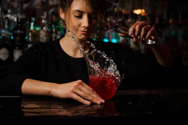 Női csapos dobott piros koktélos pohár állva a bárban counter egy jégkocka, splash — Stock Fotó