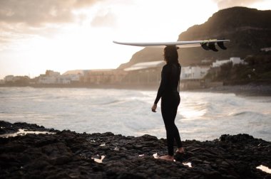 Arka görünümü esmer adam rock sahilde sunset Bulvarında okyanusa bakarak kafasına bir sörf ile ayakta.