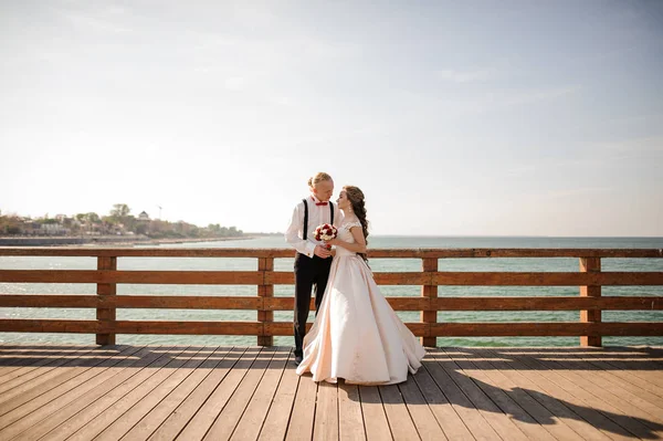 Unga vackra paret embracing på träbron i bakgrunden över havet — Stockfoto