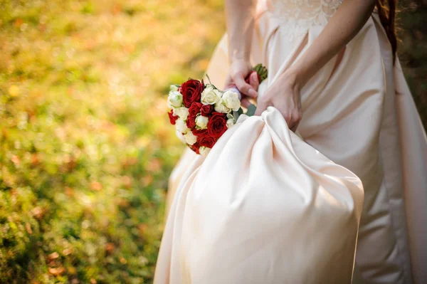 Mão de noiva segurando um vestido de noiva e buquê de flores — Fotografia de Stock