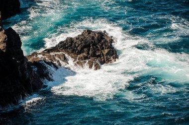 Mavi ve fırtınalı deniz kaya çevresinde beyaz dalgalar ile
