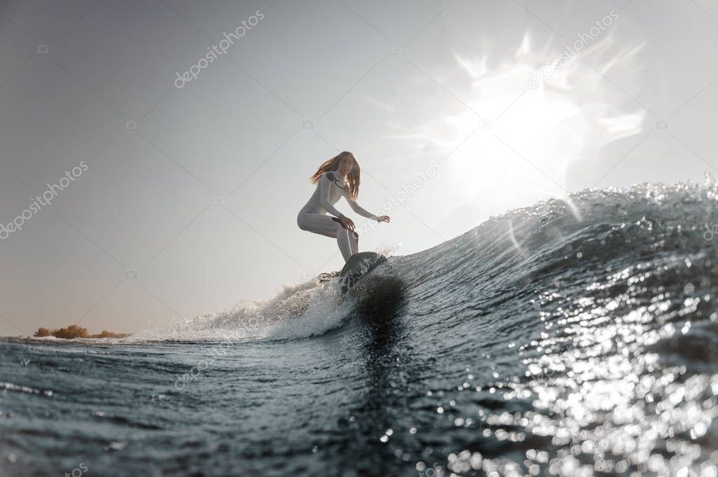 Beautiful blonde girl in the white swimsuit riding on the wakeboard on the bending knees